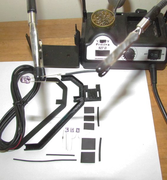 Hands soldering wires for a DIY head tracker kit with electronic components nearby.